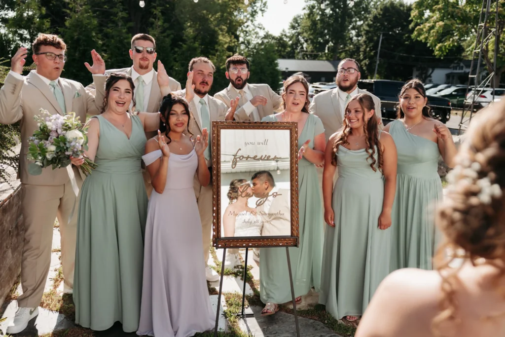 Mirror reflection of bride and groom kissing with bridal party surround the mirror cheering for a wedding at the Lockstone in Albion, New York. Captured by Wolf Cry Productions